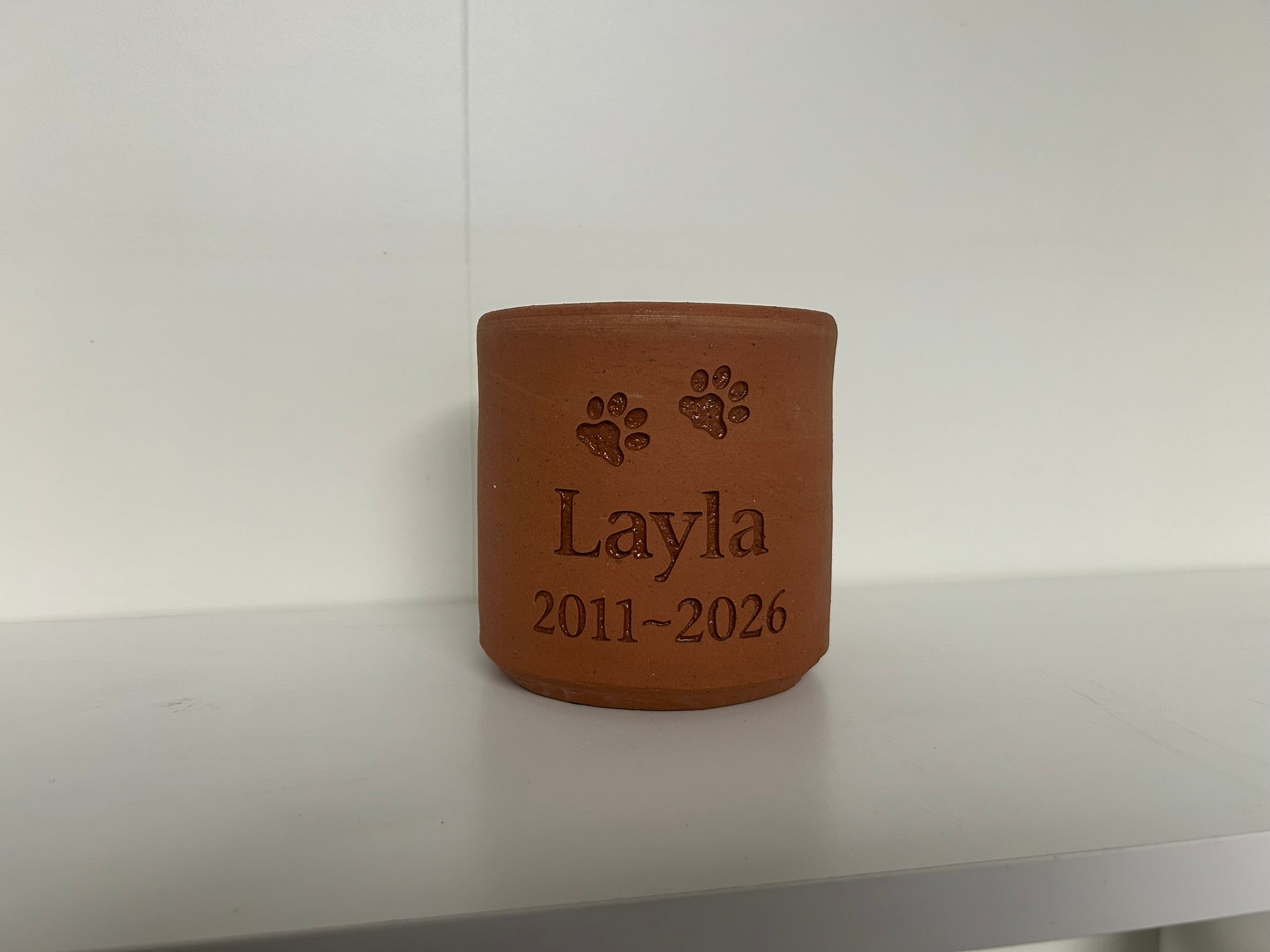 Terracotta pot with engraved name 'Layla' and years '2011-2026' on a white surface.